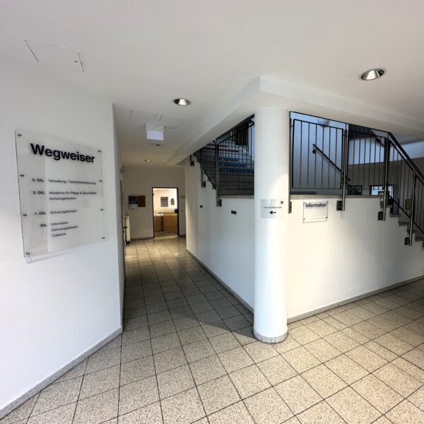Foto vom Bildungsinstitut am Zentrum Nord. Zu sehen ist der Eingangsbereich mit Treppenhaus und einem Schild auf dem Wegweiser steht.