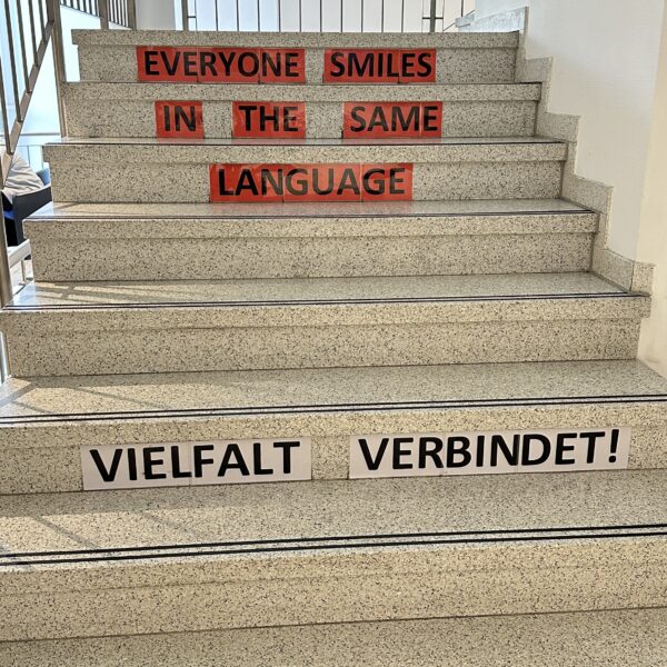 Foto der Abteilung GLA Berufssprachkurse. Zu sehen sind Treppenstufen auf denen Steht: "Vielfalt verbindet!" und "Everyone smiles in the same language".