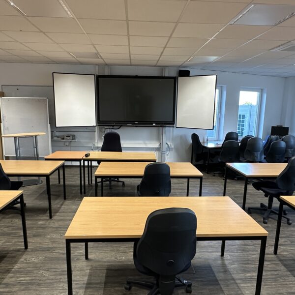 Foto von einem großen Klassenraum. Vorne hängt ein Smartboard.